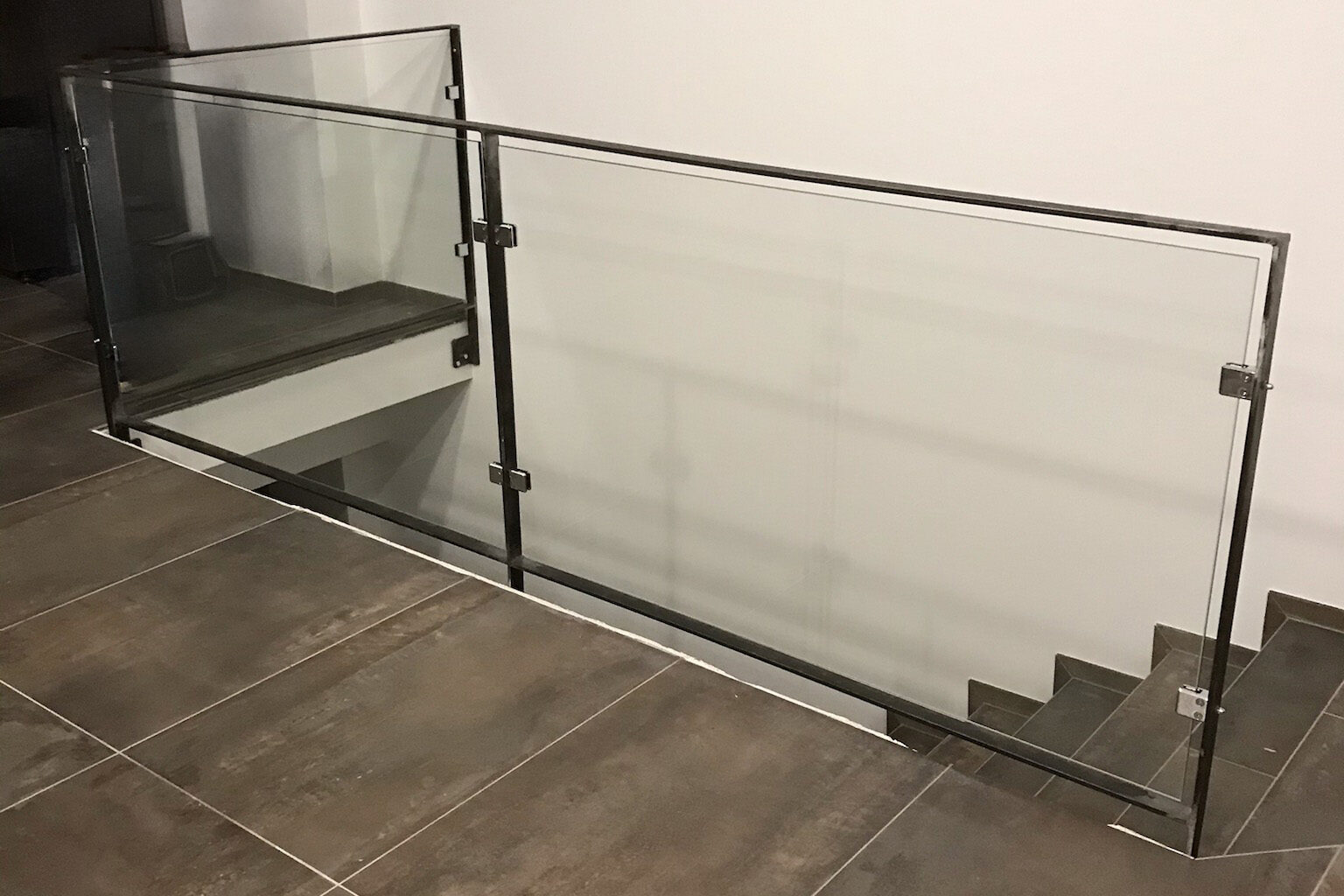 Garde-corps intérieur en verre avec structure métallique autour d’un escalier.